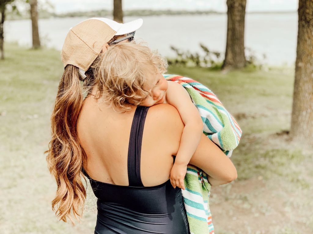 Happy mother wearing a hat showing empathy holding her toddler after swimming at the lake